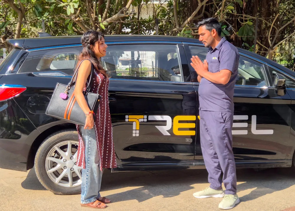 A Trevel driver greeting a passenger beside a black Trevel electric cab
